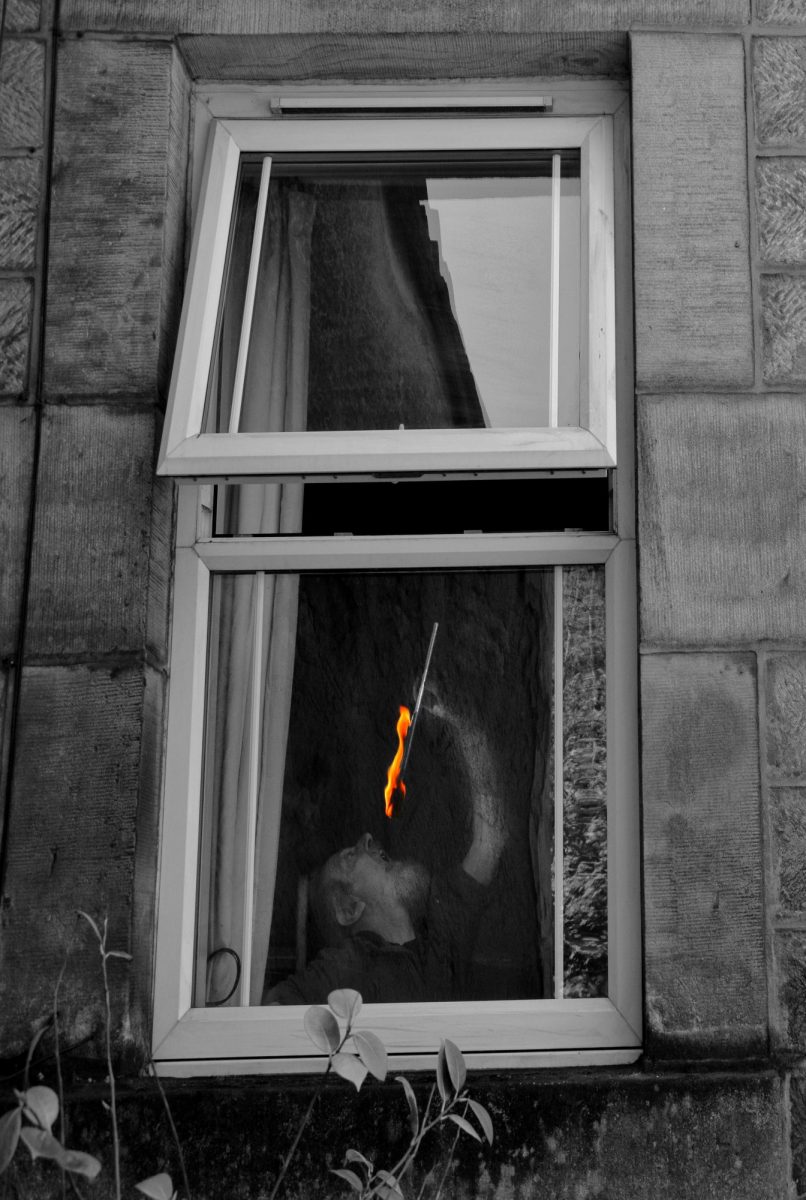 Black & White Photograph. Fire-eater performs behind a window. 