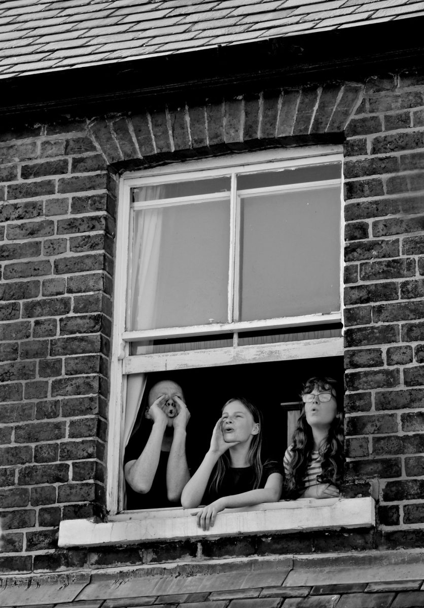 Black & White Photograph. Family lean out of upper floor window to make mooing sound.