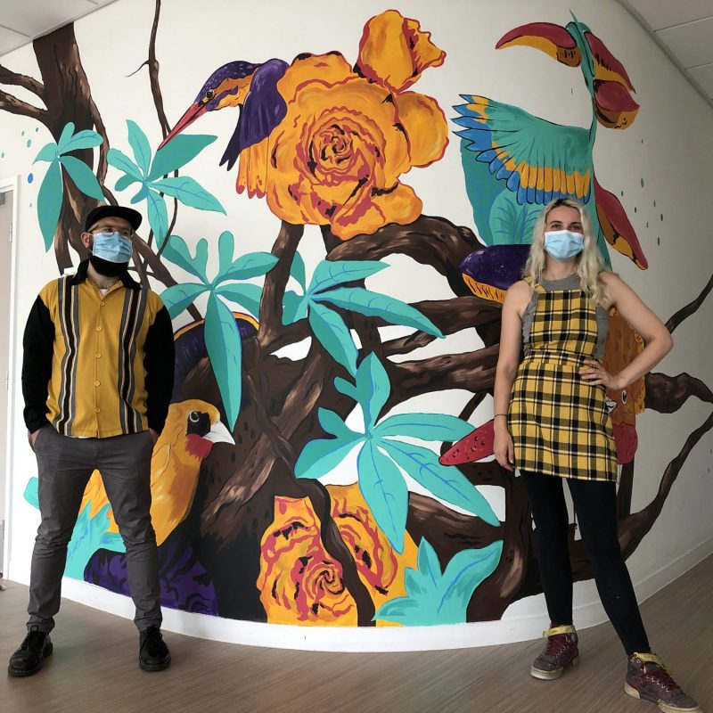 Alastair Flindall, Megan Russell standing in front of a mural featuring birds and flowers