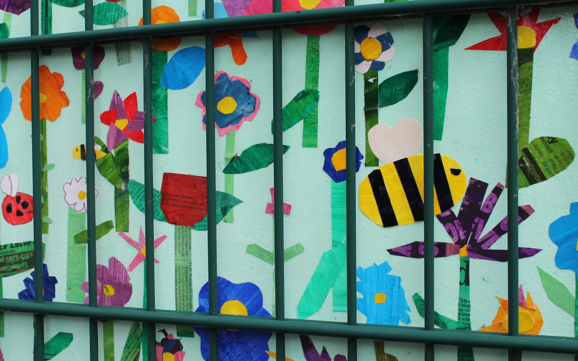 Collage artwork on a school fence, featuring flowers and bees