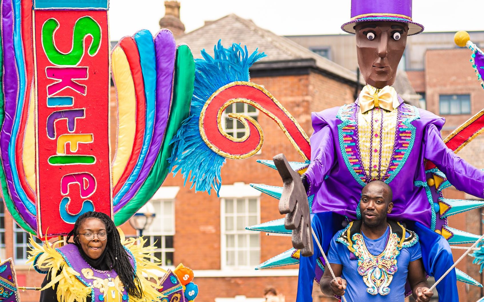 Women and man wearing carnival costumes. One based on Skittles packaging, the other a Willy Wonka Puppet.