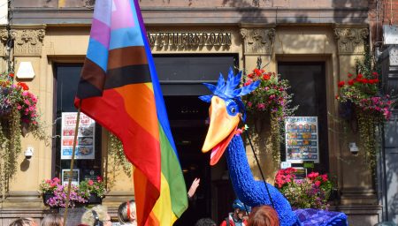 Giant blue bird puppet out side Wetherspoons at Nottingham Pride. The images also shows a crowd carrying a pride flag.