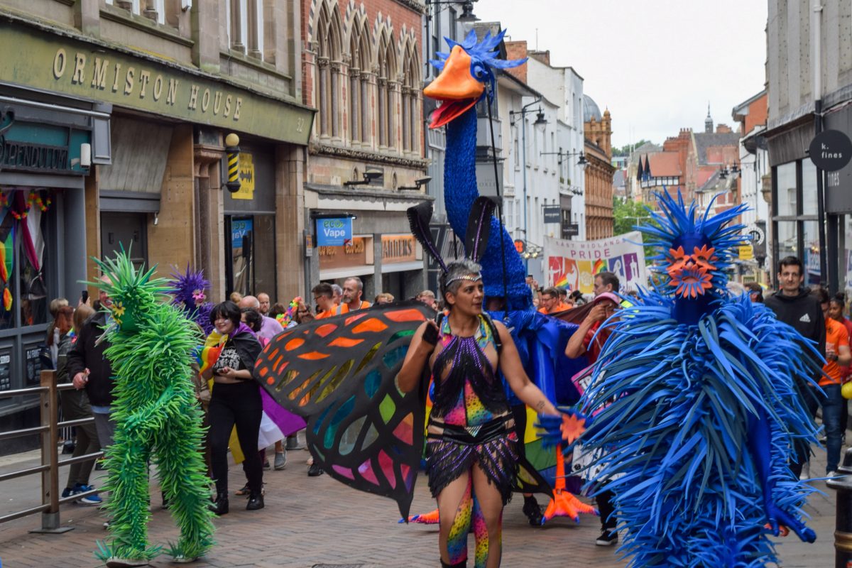 Giant blue bird puppet with carnival performers in the Nottingham pride march