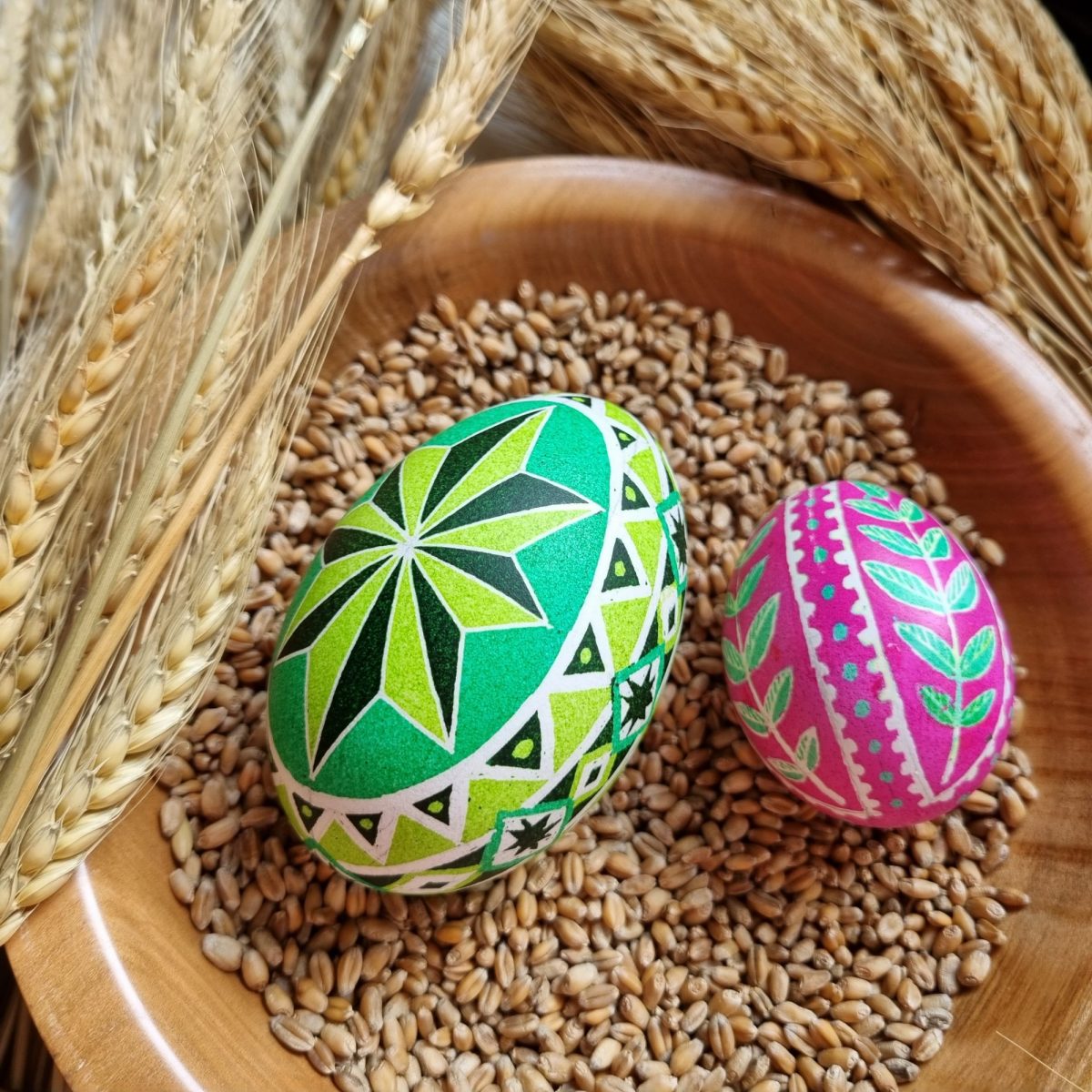 Two Pysanky-painted eggs in a grain-filled wooden bowl