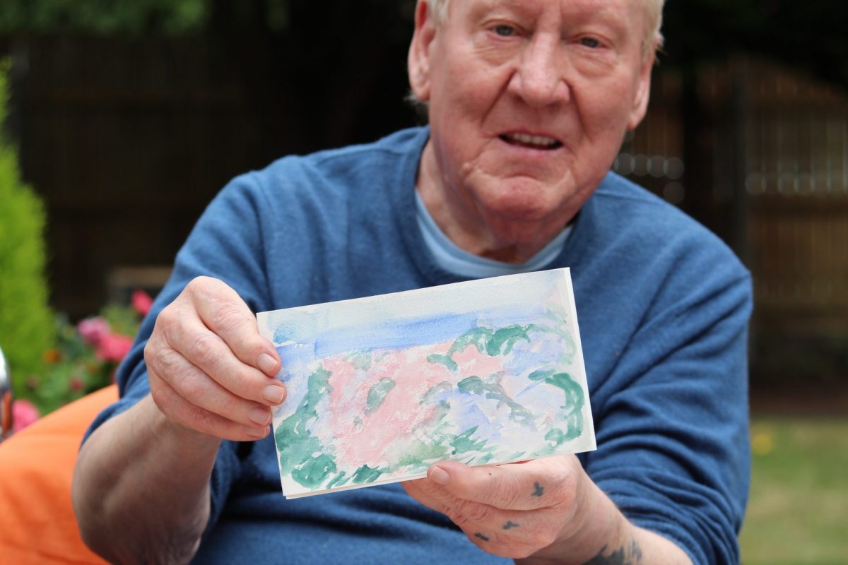 Older man holds up a watercolour sketch