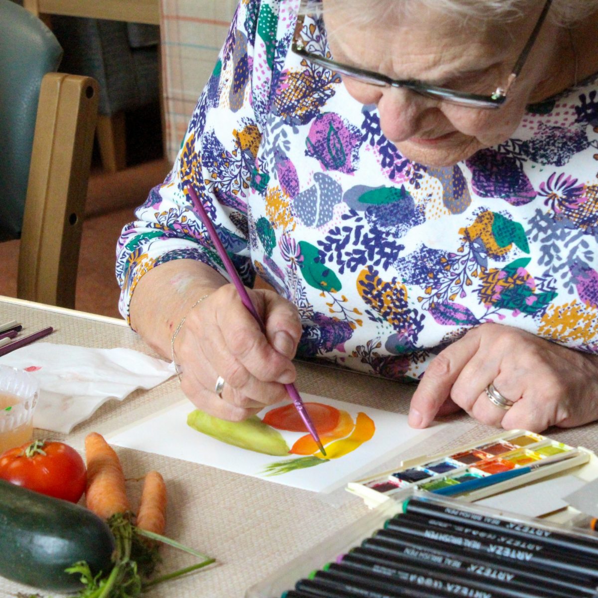 Older woman using watercolour to paint vegetables  