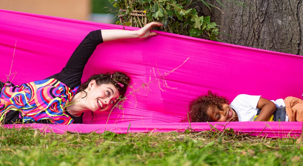 Dancer and child lie smiling in length of pink fabric