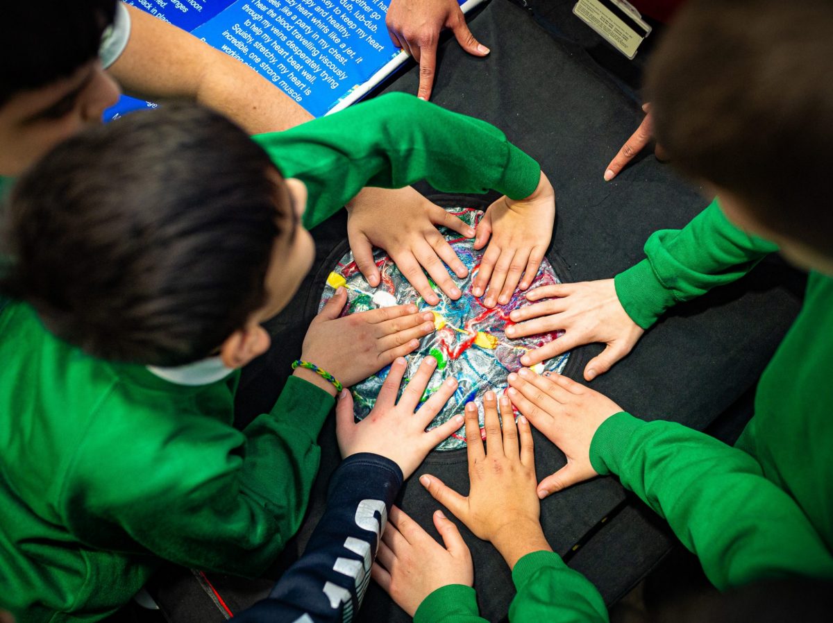 Children in green uniforms placing their hands together on a colorful, tactile educational activity mat.