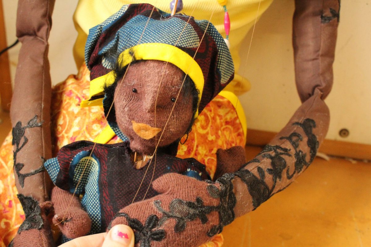 A handcrafted puppet with a patterned dress and headscarf is held up, showcasing its detailed design and texture.