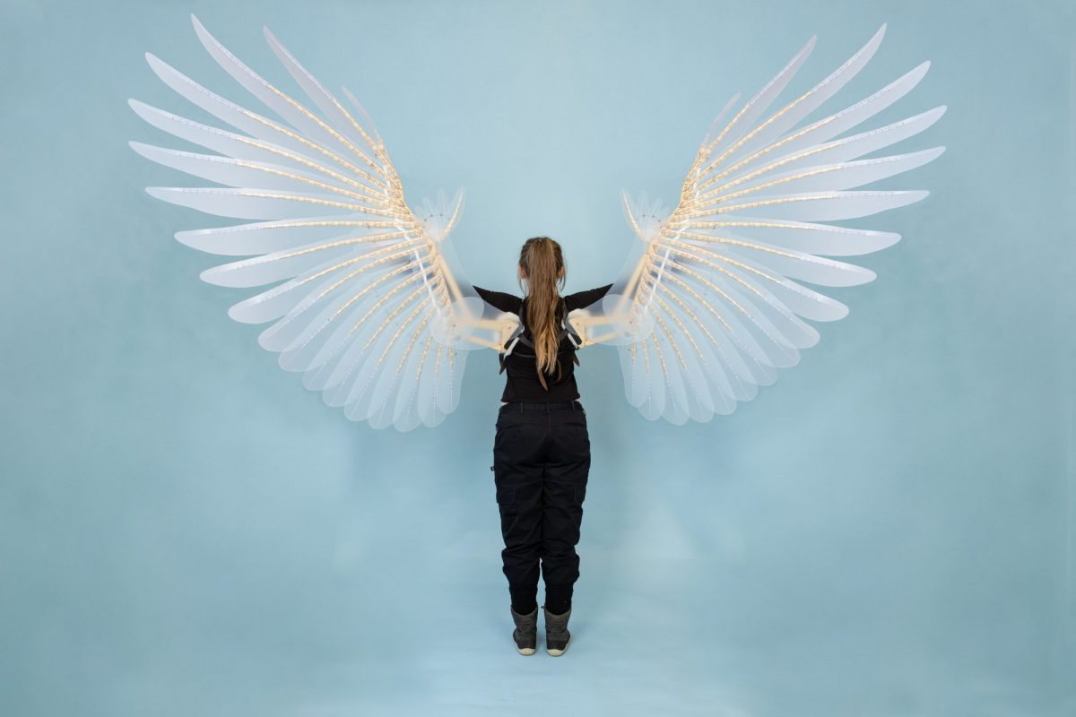 Person standing with their back to the camera wearing a large pair of illuminated white mechanical wings.