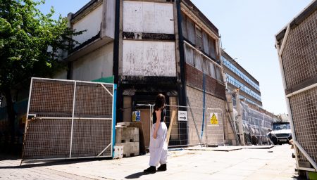 View of the boarded-up Severn’s House building in Nottingham’s Broad Marsh area, photographed before artwork begins. A person stands looking up at the building behind temporary construction fencing.