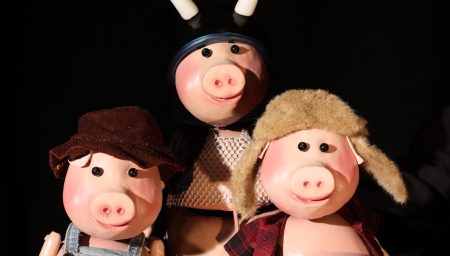 Three pig puppets wearing different costumes pose together against a black background.